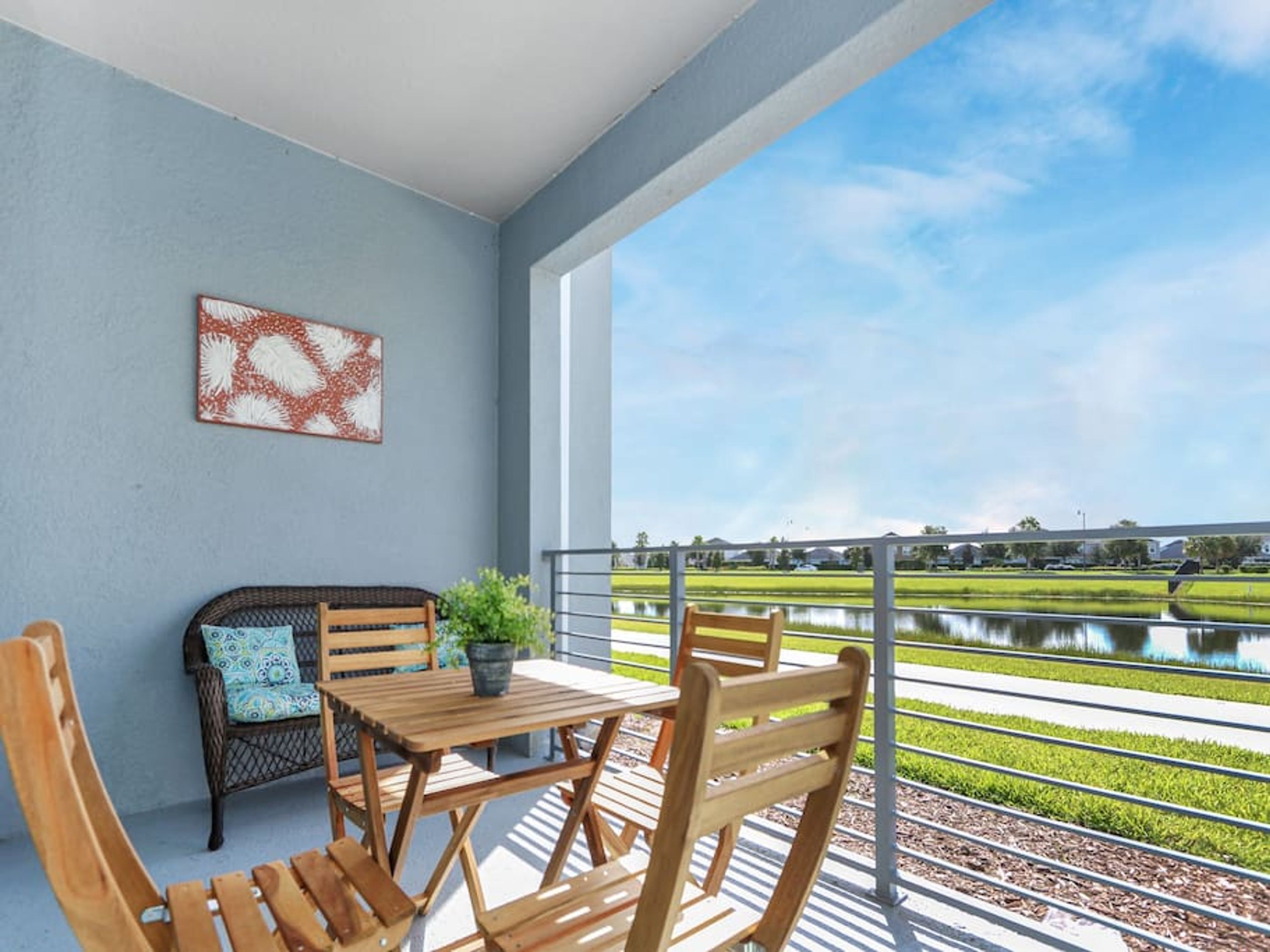 A balcony with a table and chairs, a bench with a cushion, and a view of a water body and greenery.