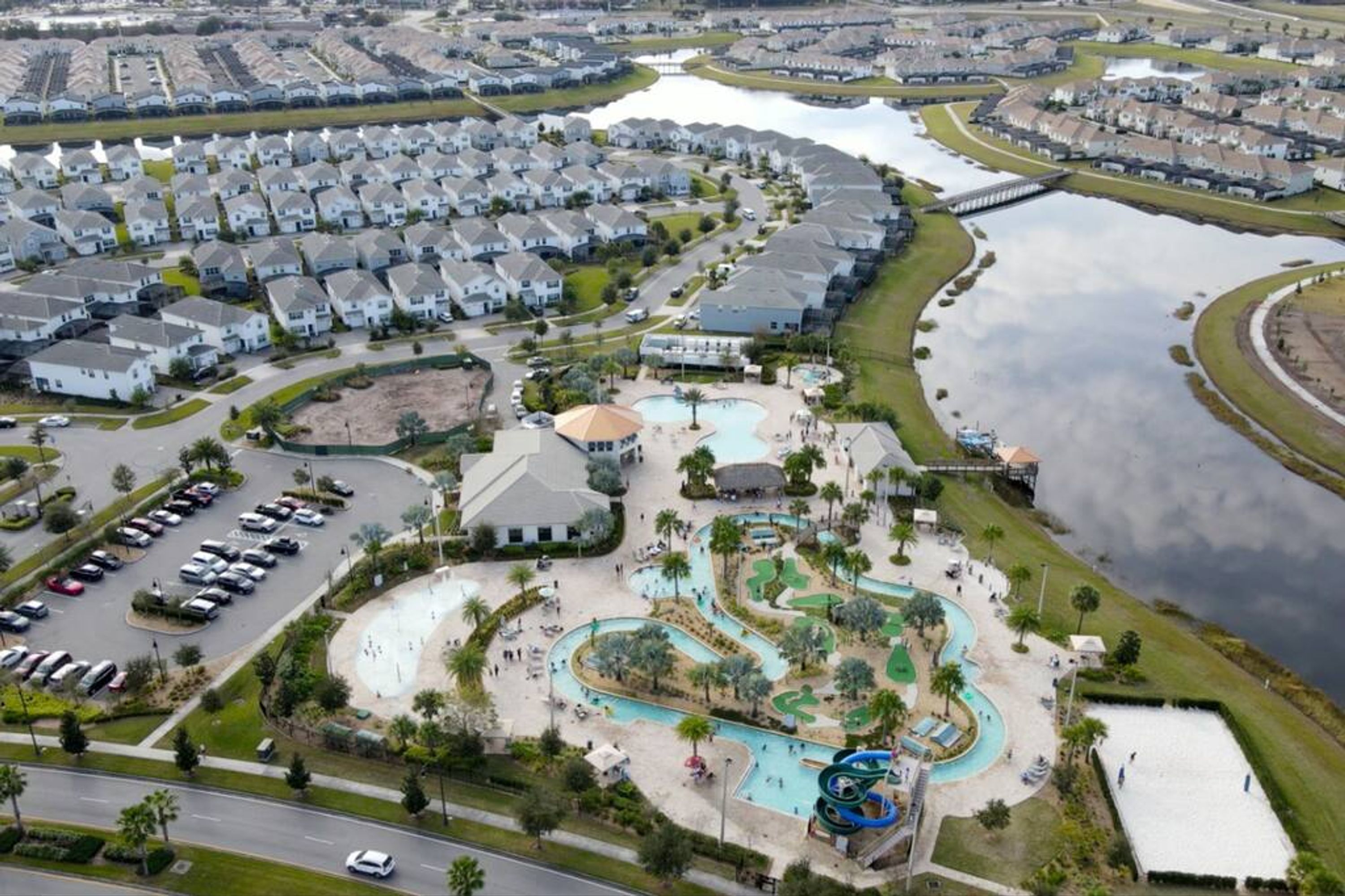 An aerial view of a residential area with a large swimming pool, a golf course, and a marina.