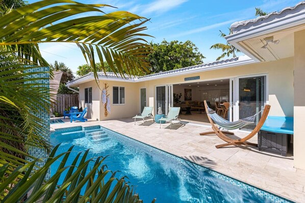 A swimming pool with lounge chairs and a hammock, surrounded by a house with a tiled patio and a covered outdoor area. - Walking Distance to the Beach 3Br House With Pool (Lauderdale-by-the-Sea)