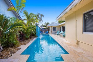 A swimming pool with a tiled deck, surrounded by palm trees and a building with a tiled roof. - Walking Distance to the Beach 3Br House With Pool (Lauderdale-by-the-Sea)