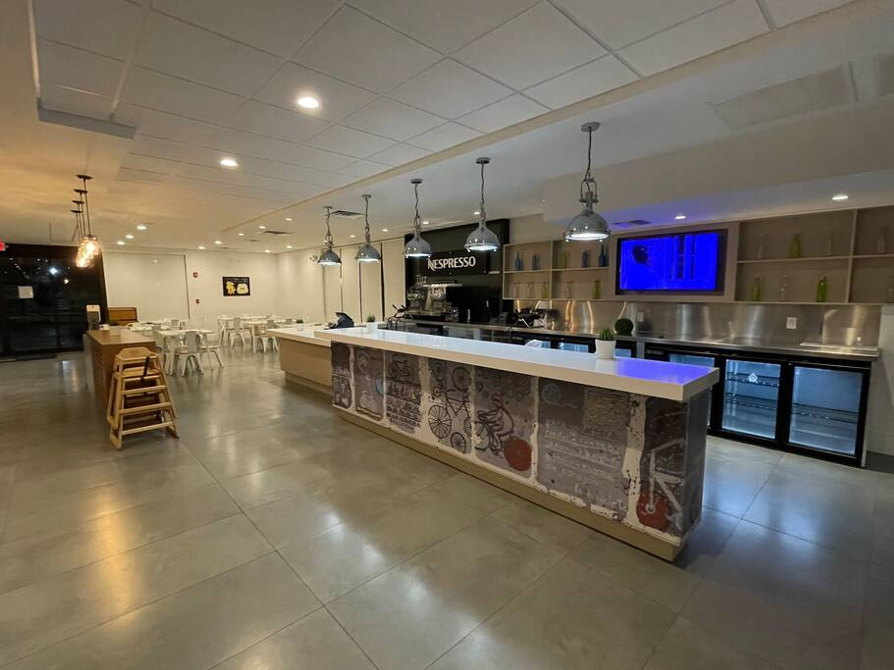 Ein modernes Café mit einer langen Theke, hängenden Pendelleuchten und einer Nespresso-Kaffeemaschine.