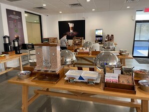 Ein Buffetbereich mit verschiedenen Speiseauslagen, darunter Müsli, Kaffee und Käse.