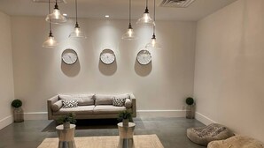 A modern living room with a beige sofa, two metal coffee tables, a round rug, and three wall clocks. - Cozy Hotel With Super Location Near Disney (Kissimmee)