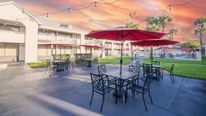 An outdoor patio with tables and chairs, red umbrellas, and string lights against a sunset sky. - Cozy Hotel With Super Location Near Disney (Kissimmee)