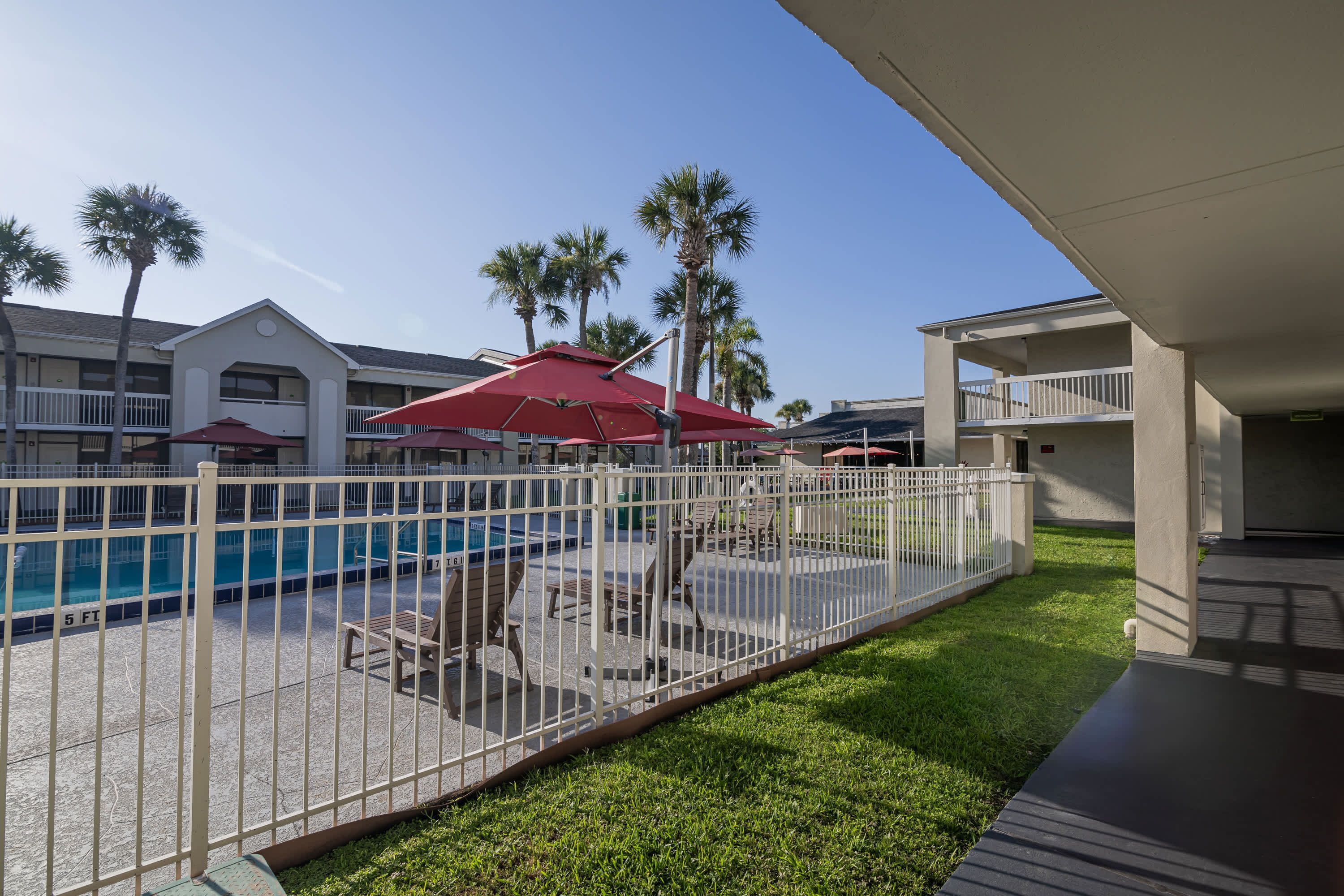 Ein Poolbereich mit umzäuntem Deck, Liegestühlen und Sonnenschirmen.