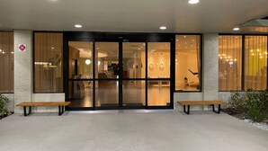 A hotel entrance with a glass door, a reception desk, and two benches outside. - Cozy Hotel With Super Location Near Disney (Kissimmee)