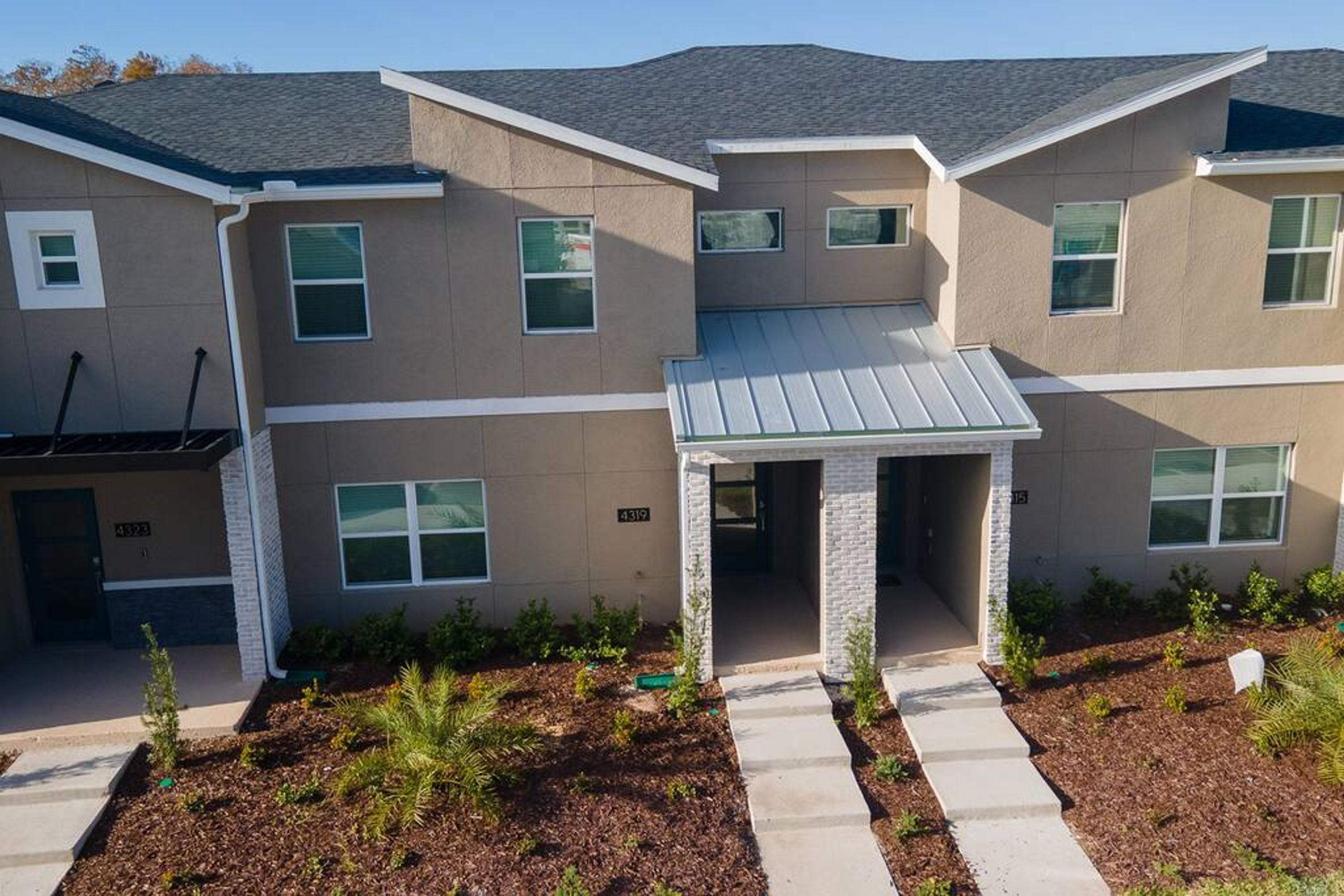 A multi-story residential building with a central entrance, a covered porch, and a landscaped front yard.