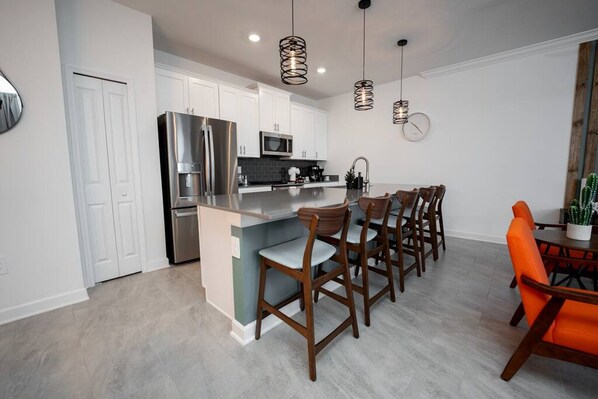 A modern kitchen with white cabinets, stainless steel appliances, and a central island with bar stools. - TH 4Br Walking Distance to Club (Kissimmee)