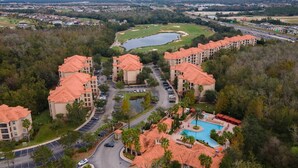 A residential complex with multiple buildings, a swimming pool, and a golf course in the background. - Tuscana Resort 3 BR Near Disney (Davenport)