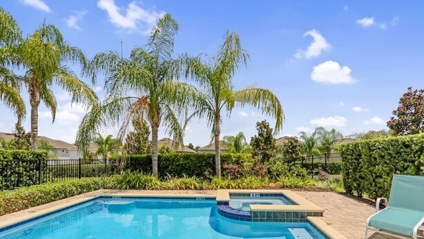 Piscina con jacuzzi, rodeada de palmeras y un jardín ajardinado.