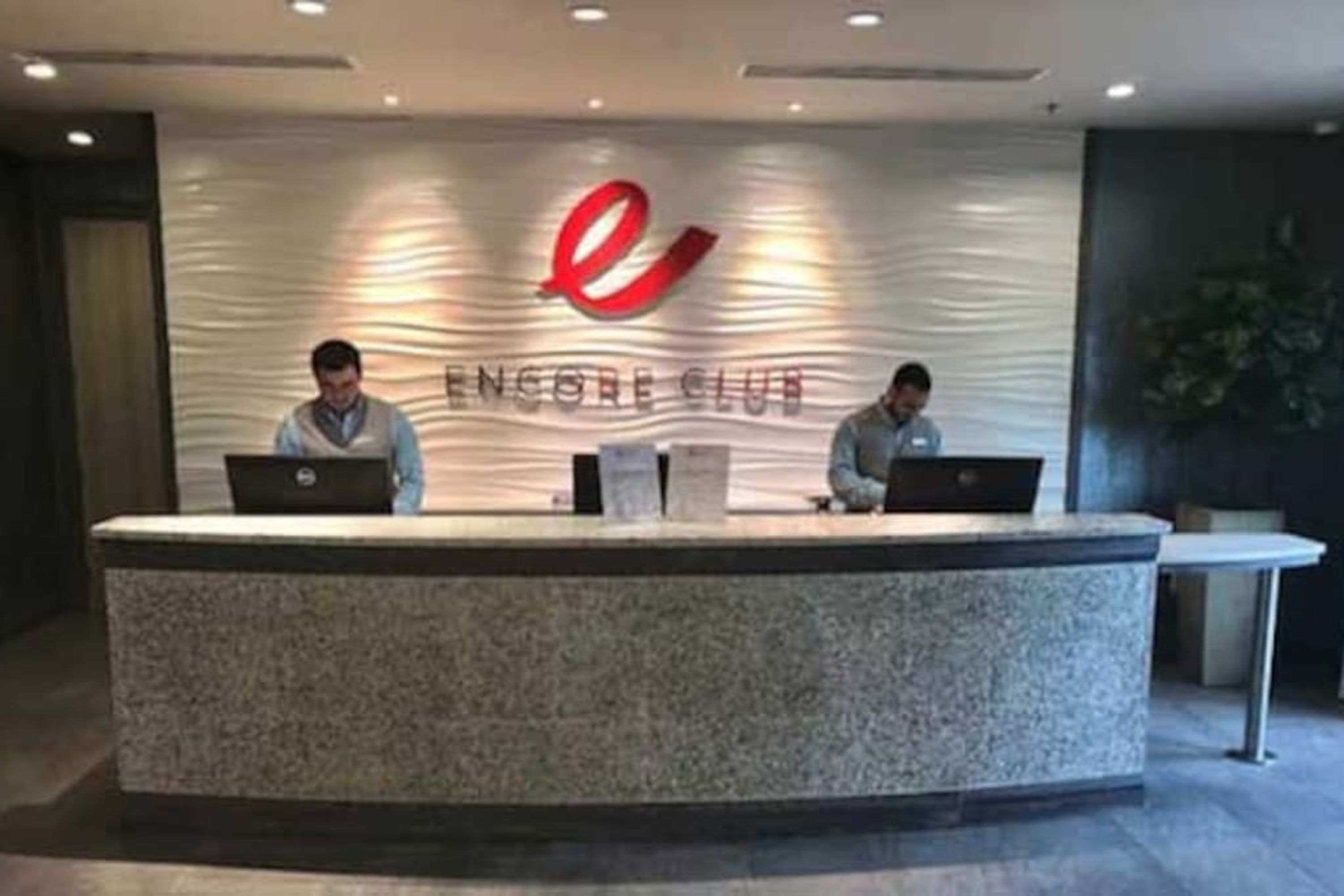 A reception desk with two staff members, laptops, and a logo for Encore Club.