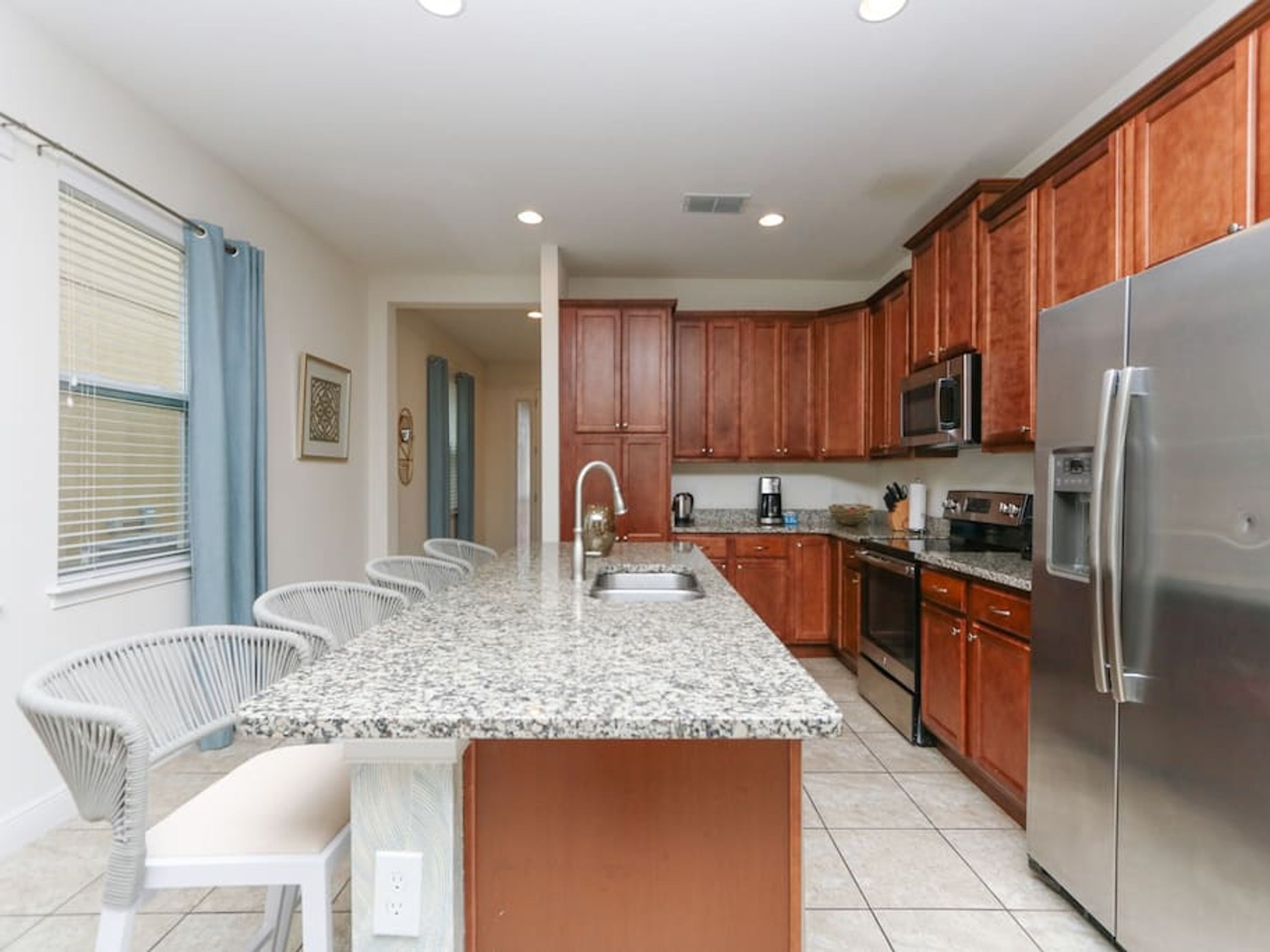 A kitchen with wooden cabinets, a stainless steel refrigerator, a granite countertop, and a built-in island with seating.