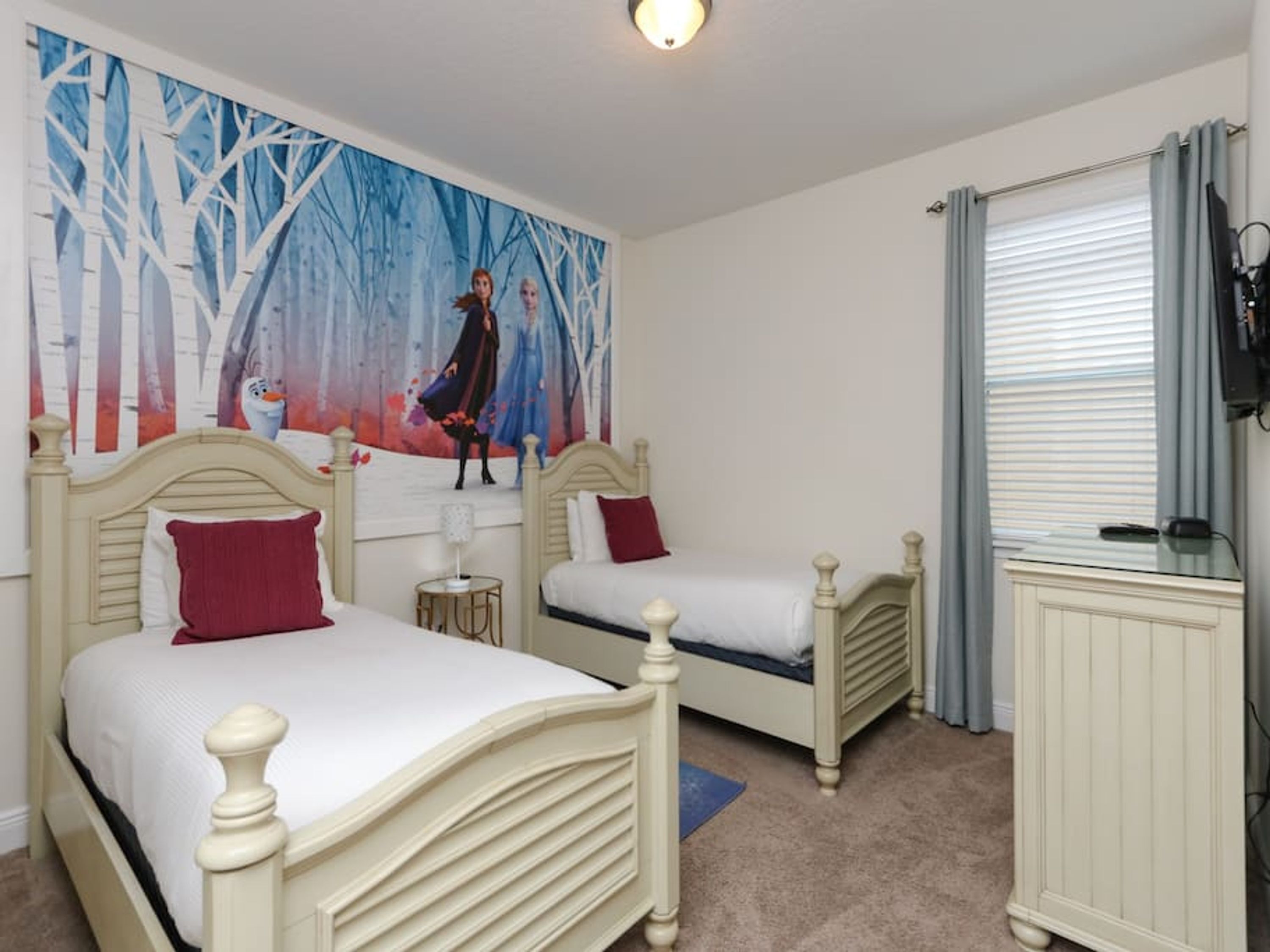 Un dormitorio con dos camas, un cuadro de un bosque nevado, un radiador y una ventana con cortinas.