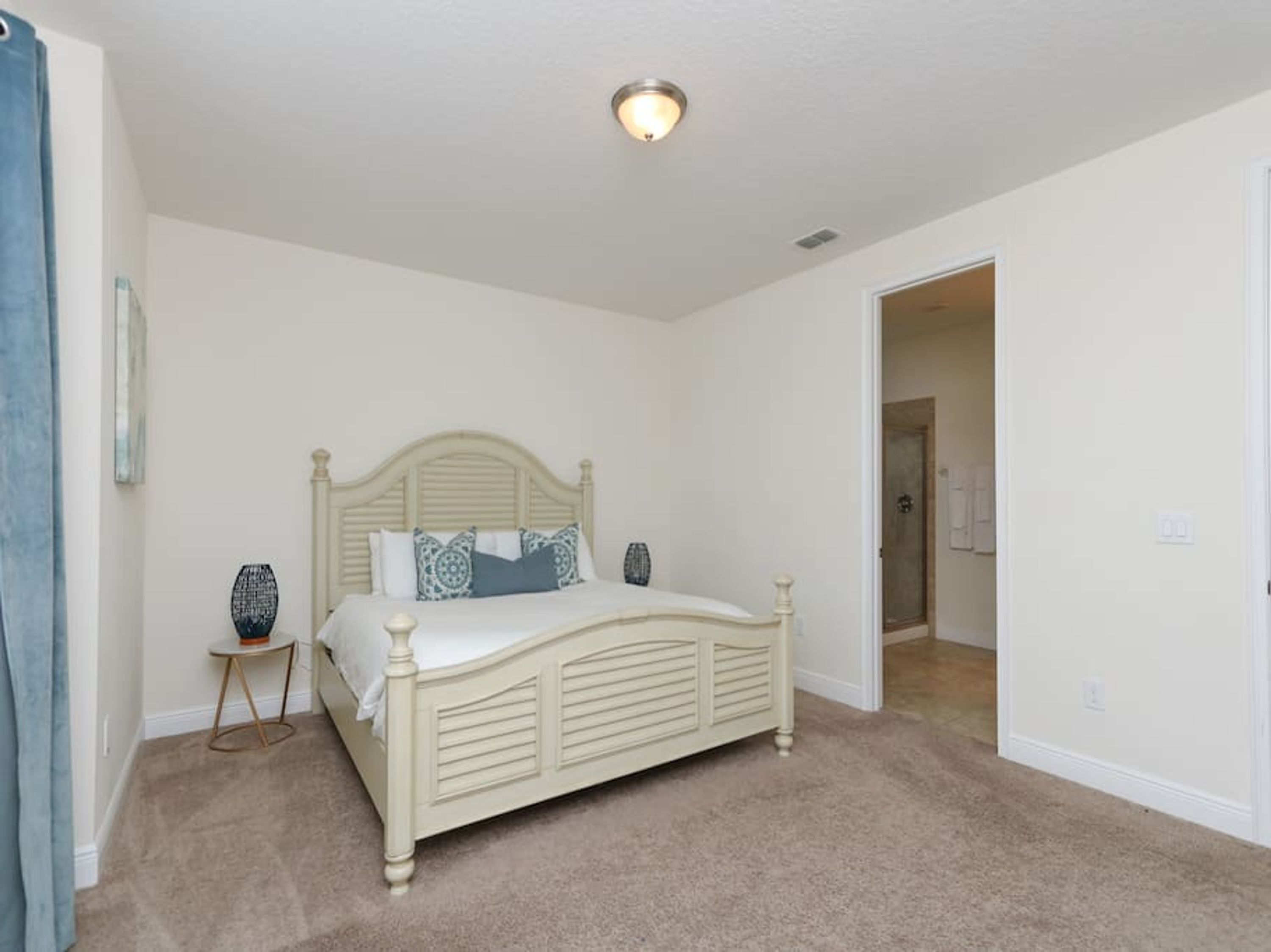 A bedroom with a bed, a small side table, and a door leading to another room.