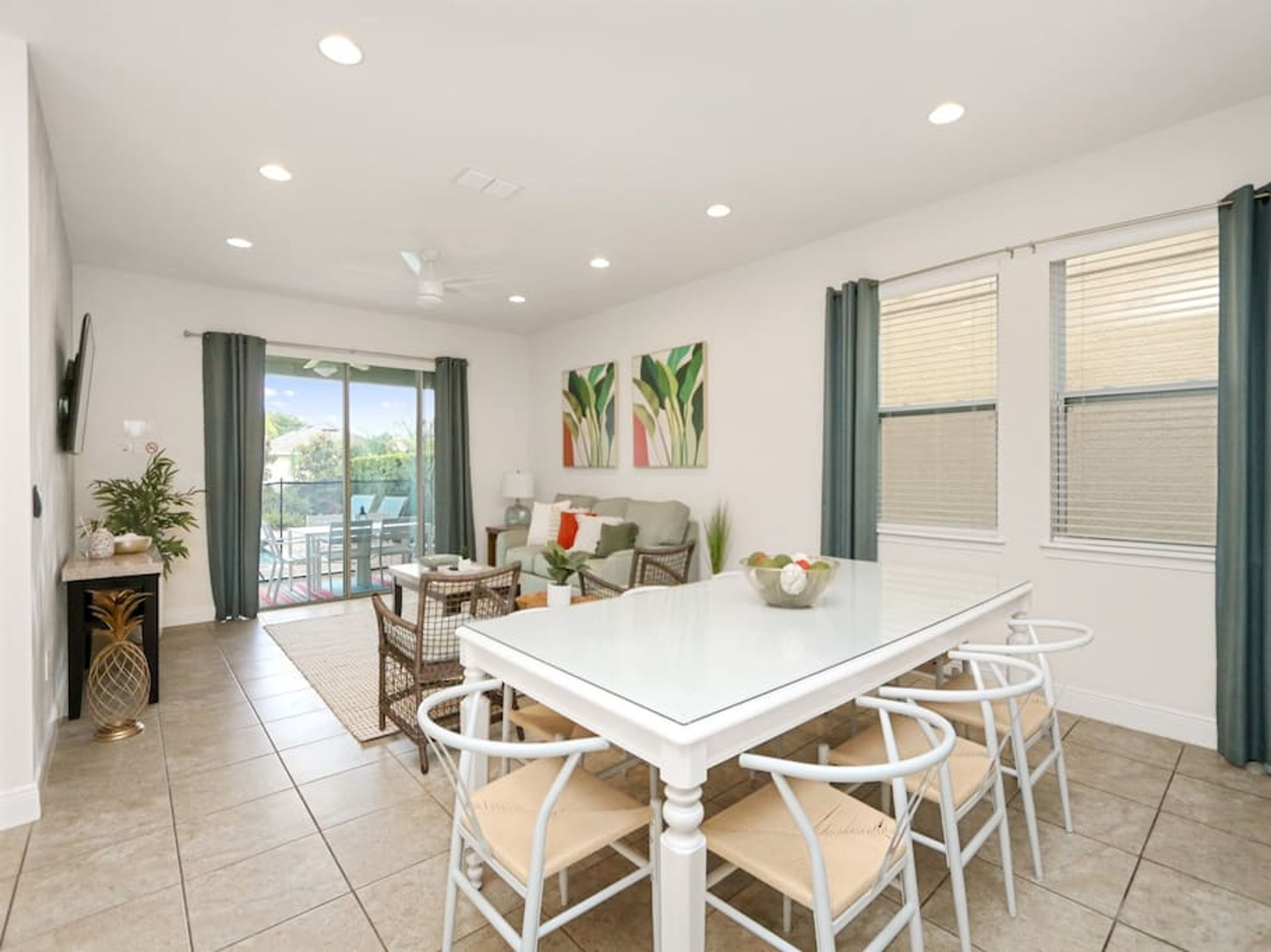 A spacious dining area with a white table and four chairs, a sofa, and a balcony with a view.