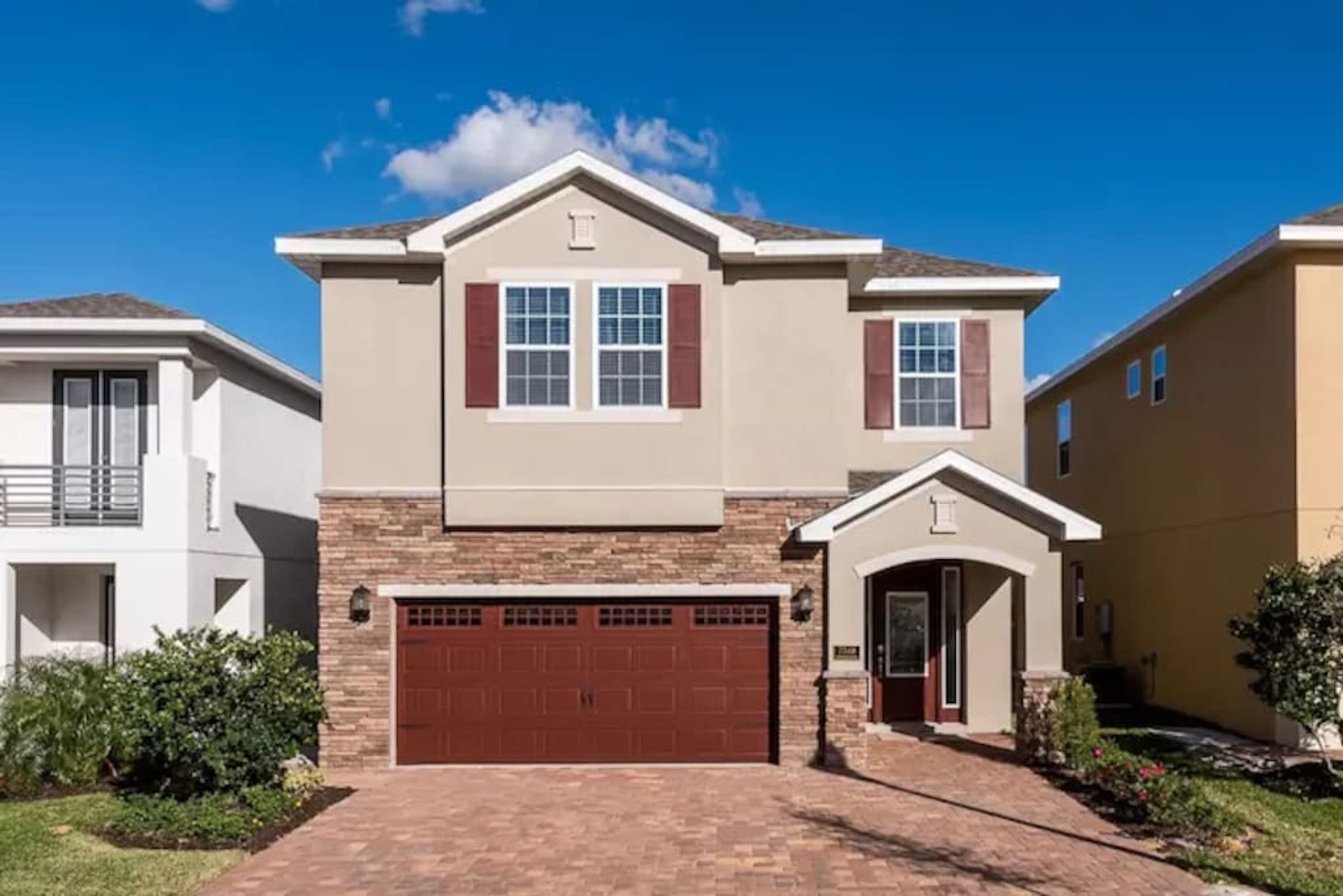 A two-story residential building with a brick driveway, a garage, and a small front porch.