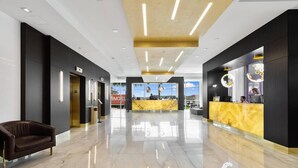 A modern hotel lobby with a reception desk, a sofa, and a view of the cityscape through large windows. - Amazing Condo in Hollywood Beach (Hollywood)