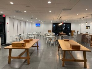 Ruime eethoek met meerdere tafels en stoelen, een televisiescherm aan de muur en een modern plafondontwerp.