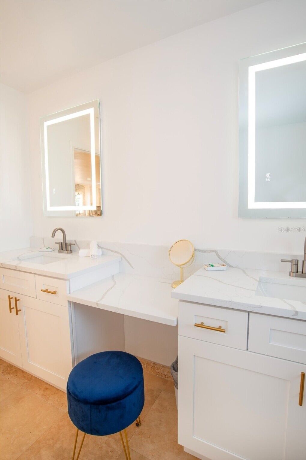 A modern bathroom with two sinks, a vanity, and a blue stool.
