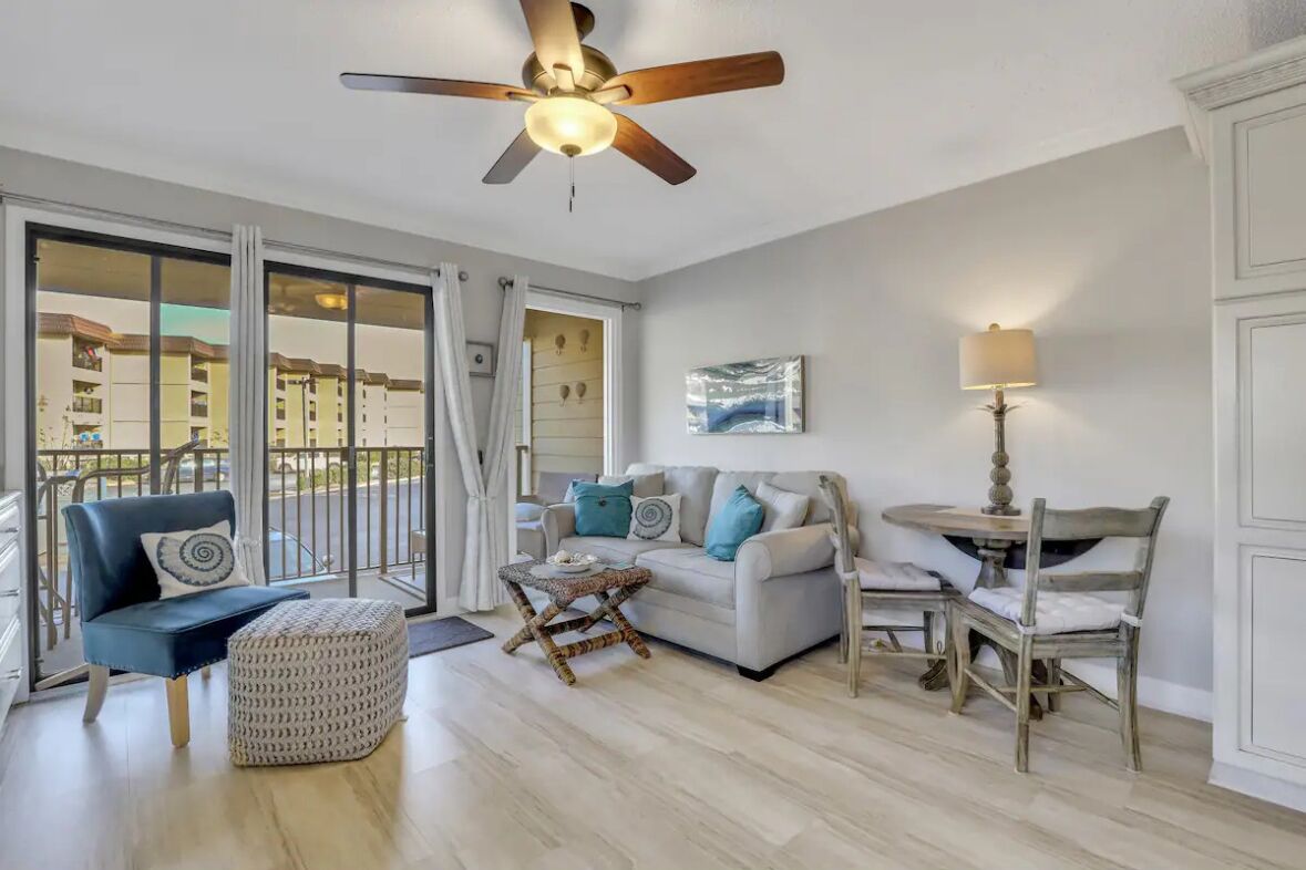 A living room with a sofa, a chair, a table, and a ceiling fan.