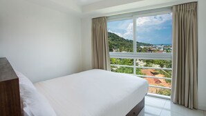 Una habitación de hotel con un ventanal grande, una cama y una mesita de noche de madera.