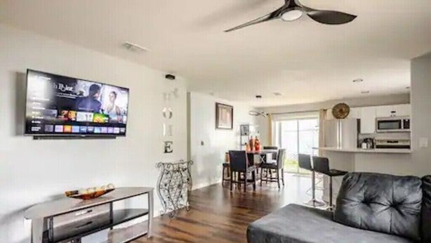 A modern living room with a flat-screen TV, a grey sofa, and a dining area with a table and chairs. - Royal Rose Dream Getaway (Tampa)