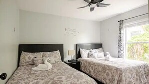 A bedroom with two beds, a ceiling fan, a nightstand, and a window with curtains. - Royal Rose Dream Getaway (Tampa)