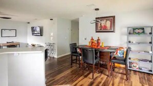 A modern living room with a dining area, wooden flooring, and a TV mounted on the wall. - Royal Rose Dream Getaway (Tampa)