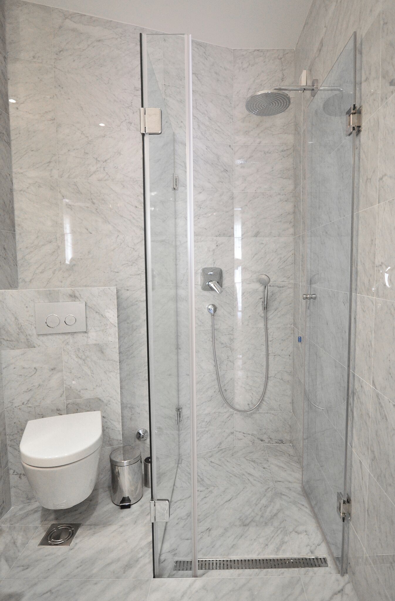 Une salle de bain moderne avec une douche à parois de verre, des toilettes et une poubelle.