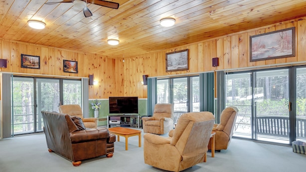 Una sala de estar con paneles de madera, sofás de cuero, una mesa de centro y un televisor. Amplias ventanas ofrecen vistas al exterior.