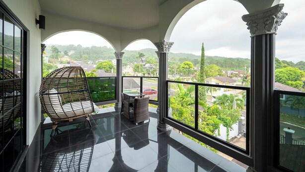 A balcony with a glass table and chairs, overlooking a residential area with houses and greenery. - One Love Guesthouse (Montego Bay)