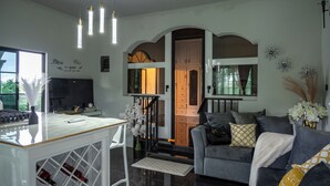 A modern living room with a grey sofa, a white coffee table, and a TV. There is a staircase leading to a wooden door. - One Love Guesthouse (Montego Bay)