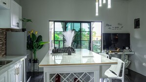 A modern kitchen with a central island, white cabinetry, and a large window offering a view of greenery outside. - One Love Guesthouse (Montego Bay)