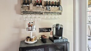 A bar area with a wine rack, glasses, a coffee station, and a sign that reads "But First Coffee".