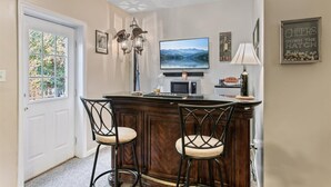 A bar area with a TV, bar stools, a lamp, and a sign saying "Cheers Down the Hatch".