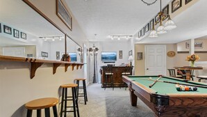 A pool room with a pool table, bar stools, and a bar area.