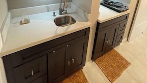 A compact kitchen with a sink, dark cabinets, and a stove.
