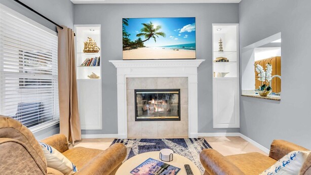 A living room with a fireplace, a flat-screen TV mounted above it, and a bookshelf with decorative items. - Waterfront, Boat Dock, Kayaks, Fishing, Pool, Spa. 4BR / 9Beds / Sleeps14 (Palmetto)