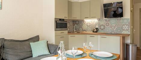 A modern kitchen with a dining area, including a wooden table set for four, a sofa, and a kitchen counter with a tiled backsplash.