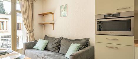 A modern living room with a grey sofa, wooden table, and a built-in oven.