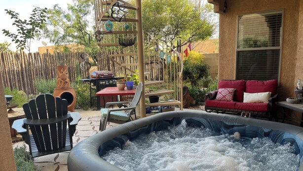Un jacuzzi dans un jardin, avec une clôture en bois, un barbecue et du mobilier d’extérieur.