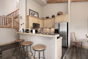 Una cocina con armarios de madera, un refrigerador de acero inoxidable, un microondas y dos taburetes de bar.