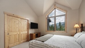 A bedroom with a large window, a bed, a TV, and wooden wardrobes. - Lakota Lookout | 4BR Hot Tub, Across from Resort (Winter Park)