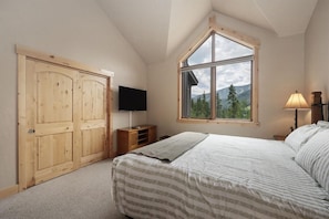 A bedroom with a large window, a bed, a TV, and wooden wardrobes.