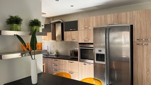 A modern kitchen with wooden cabinets, a stainless steel refrigerator, and a black countertop. - Artistic 2-bedroom apartment in green & peaceful Vari (Vari)