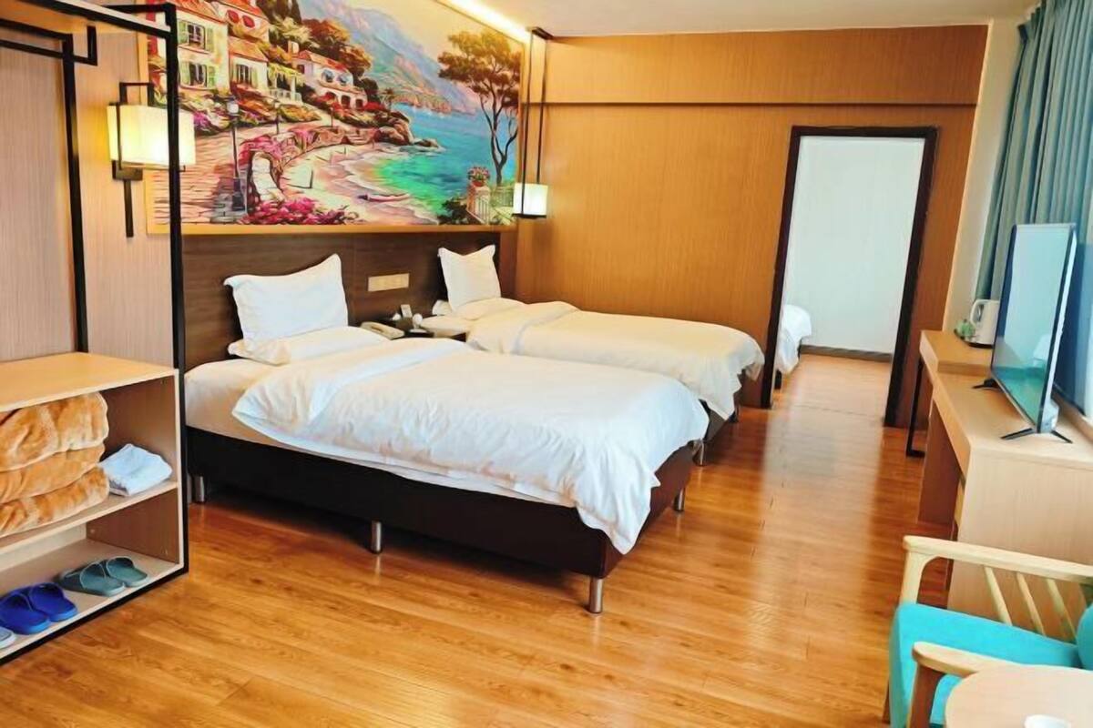 Une chambre d’hôtel avec deux lits, un plancher en bois, un tableau au mur, une télévision et un bureau avec une chaise.