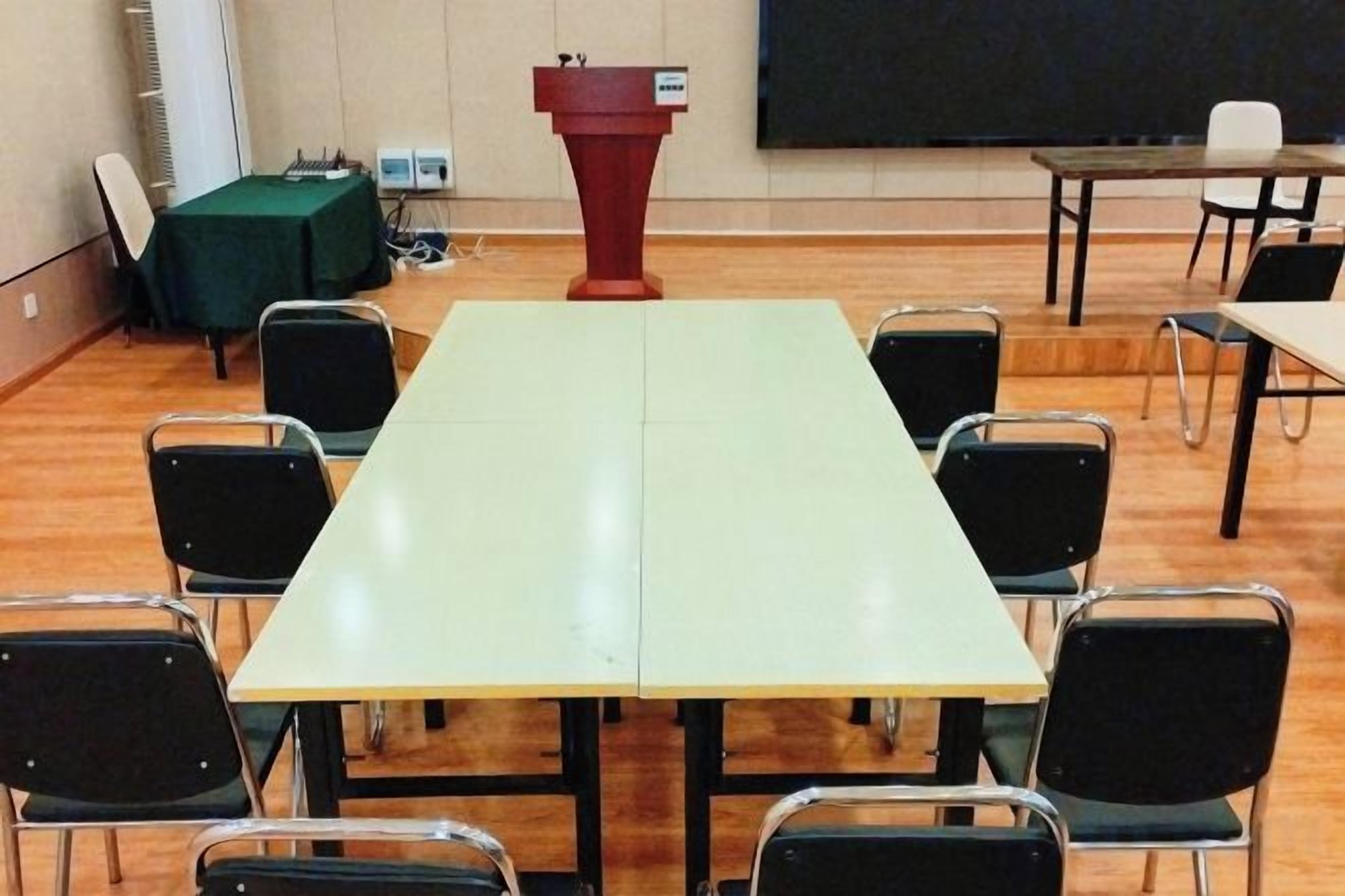 Une salle de conférence avec une longue table, des chaises, un pupitre et un tableau noir.