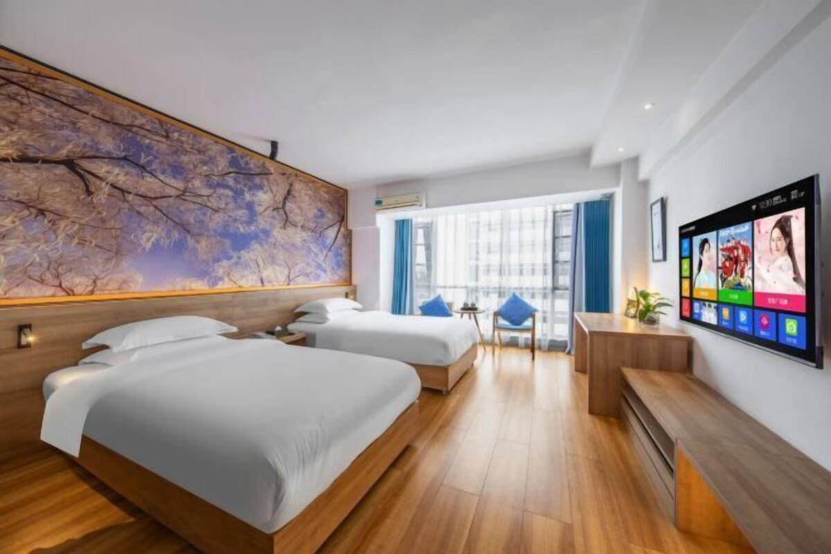 Une chambre d’hôtel avec deux lits, une grande fresque murale, une télévision et un balcon avec vue.