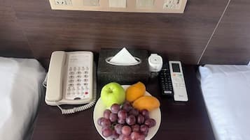 Ein Hotelzimmer mit einem Nachttisch, der ein Telefon, eine Papiertasche, eine Fernbedienung und eine Fruchtschale enthält.