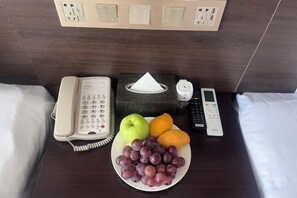 Ein Hotelzimmer mit einem Nachttisch, der ein Telefon, eine Papiertasche, eine Fernbedienung und eine Fruchtschale enthält.